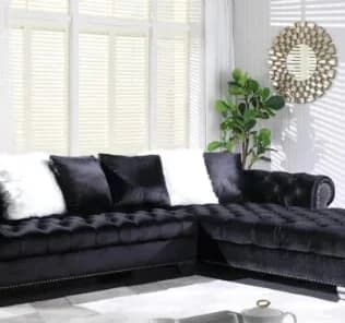 Black velvet L-shaped sectional sofa with pillows in bright living room, 16% off sale price $1,599