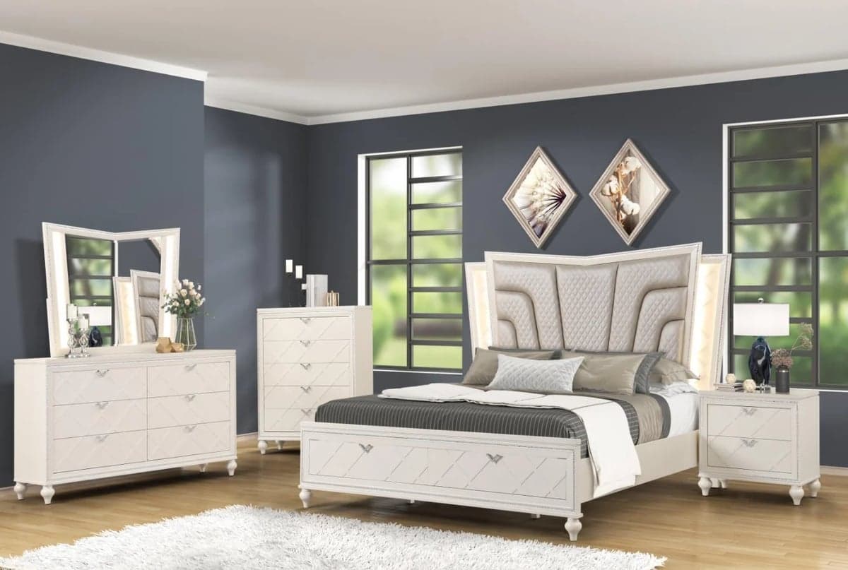 Modern bedroom furniture set with white upholstered bed, matching nightstands and dresser against dark blue walls with windows.