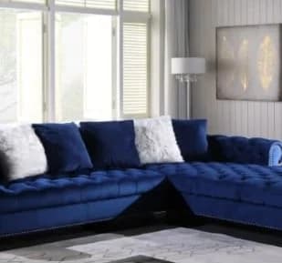 Navy blue velvet L-shaped sectional sofa with white and blue pillows in a bright living room with large windows