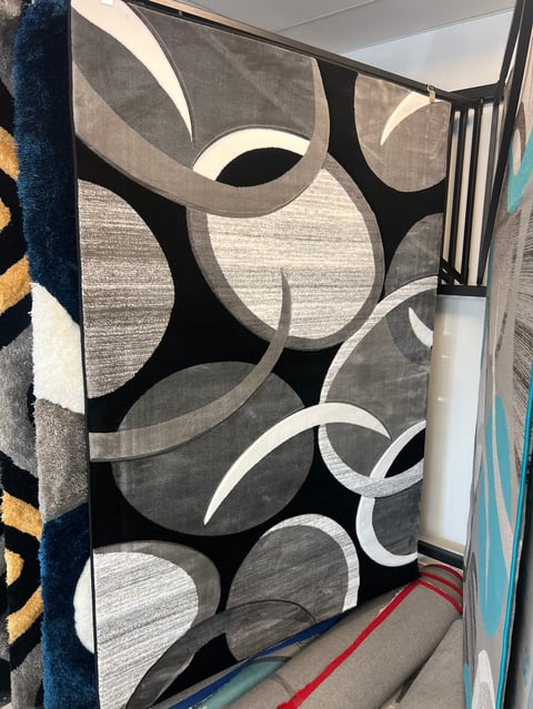 Display of modern area rugs with abstract geometric patterns in black, gray, and white tones