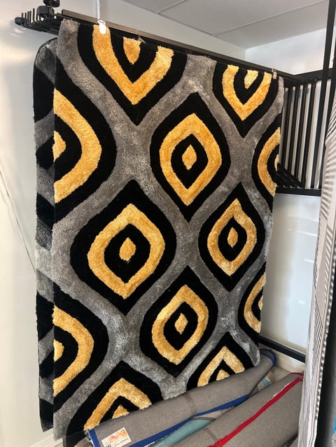 Gray area rug with yellow and black geometric diamond pattern displayed on a rack