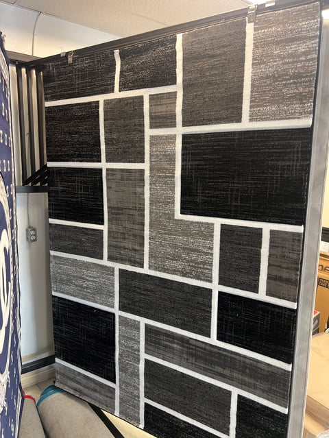Display of black and gray textured fabric samples arranged in a white-framed grid pattern on a showroom wall