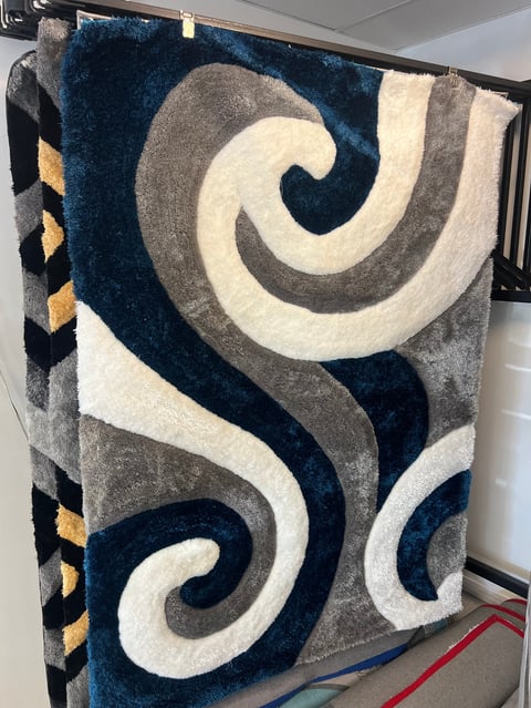 Modern area rug with abstract swirl design in navy blue, gray, cream, and gold tones displayed indoors