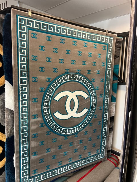 Luxury designer rug with CC logo center medallion, Greek key border, and repeating pattern on teal and beige background