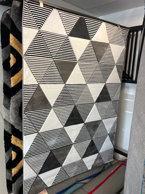 Geometric black and white striped triangular pattern rug displayed in a showroom with other textiles visible on the sides