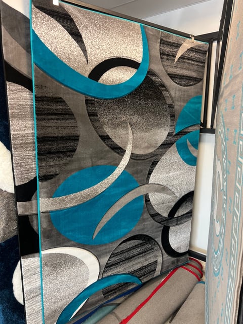 Display of decorative area rugs with geometric patterns in turquoise, gray, black, and white colors
