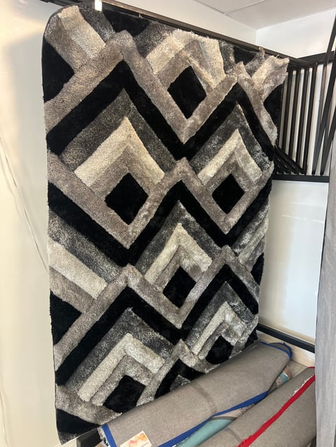 Black and gray geometric patterned area rug leaning against wall in home interior